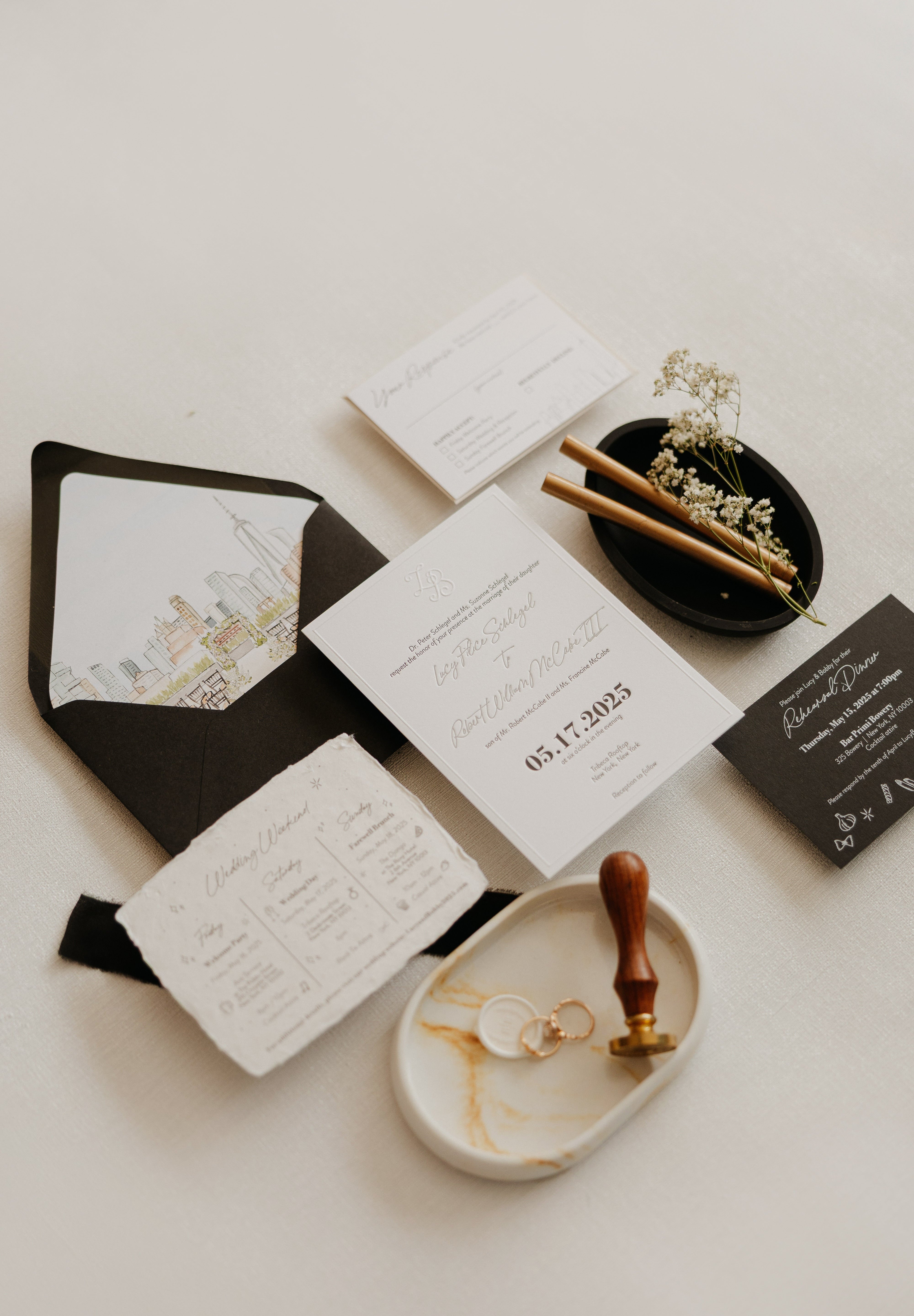 A flat lay of a black and white invitation suite. The black envelope has a watercolor illustration of the New York City skyline on the inside flap.