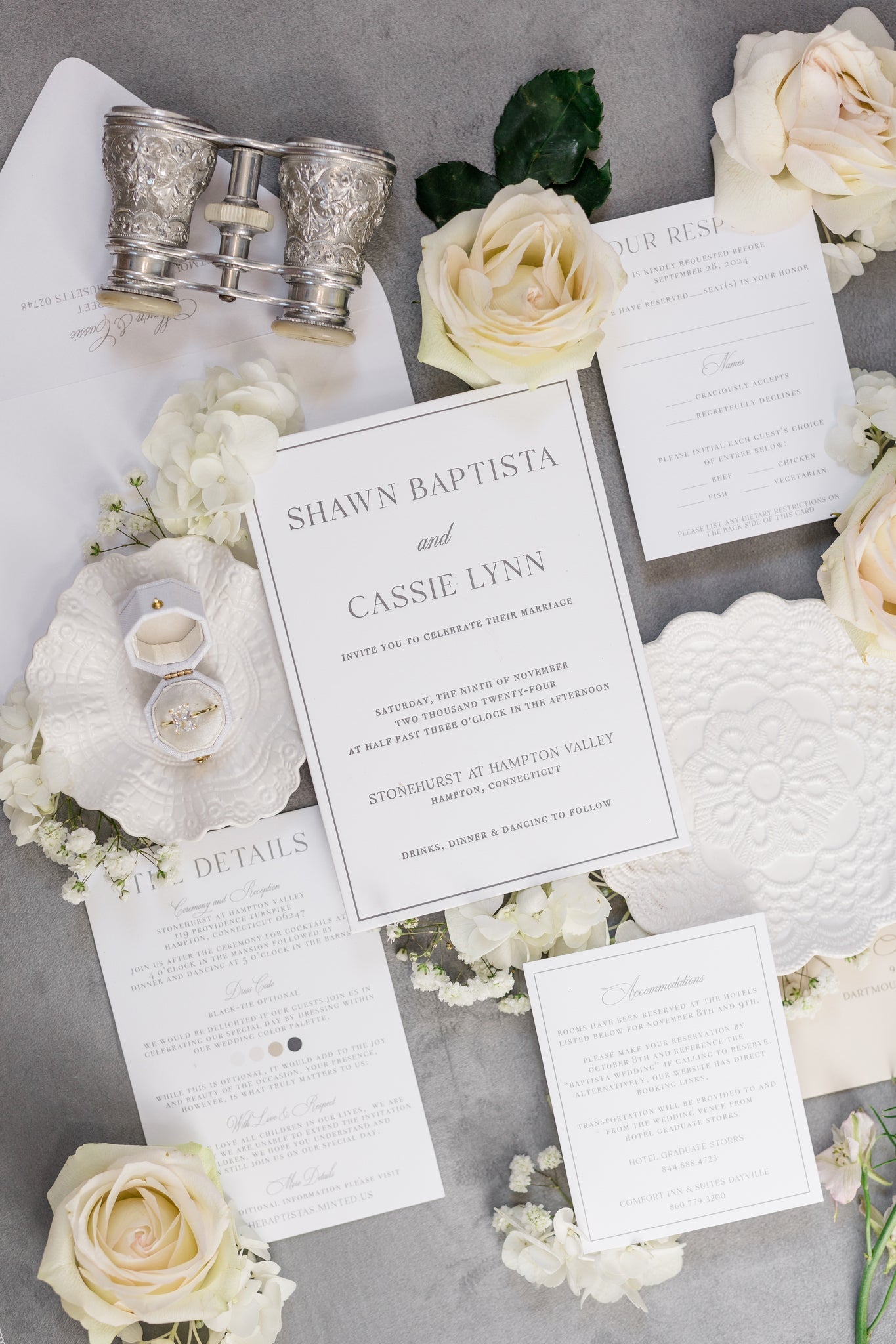 A flat lay of a wedding suite. The invites are printed on white card stock with simple gray text print.