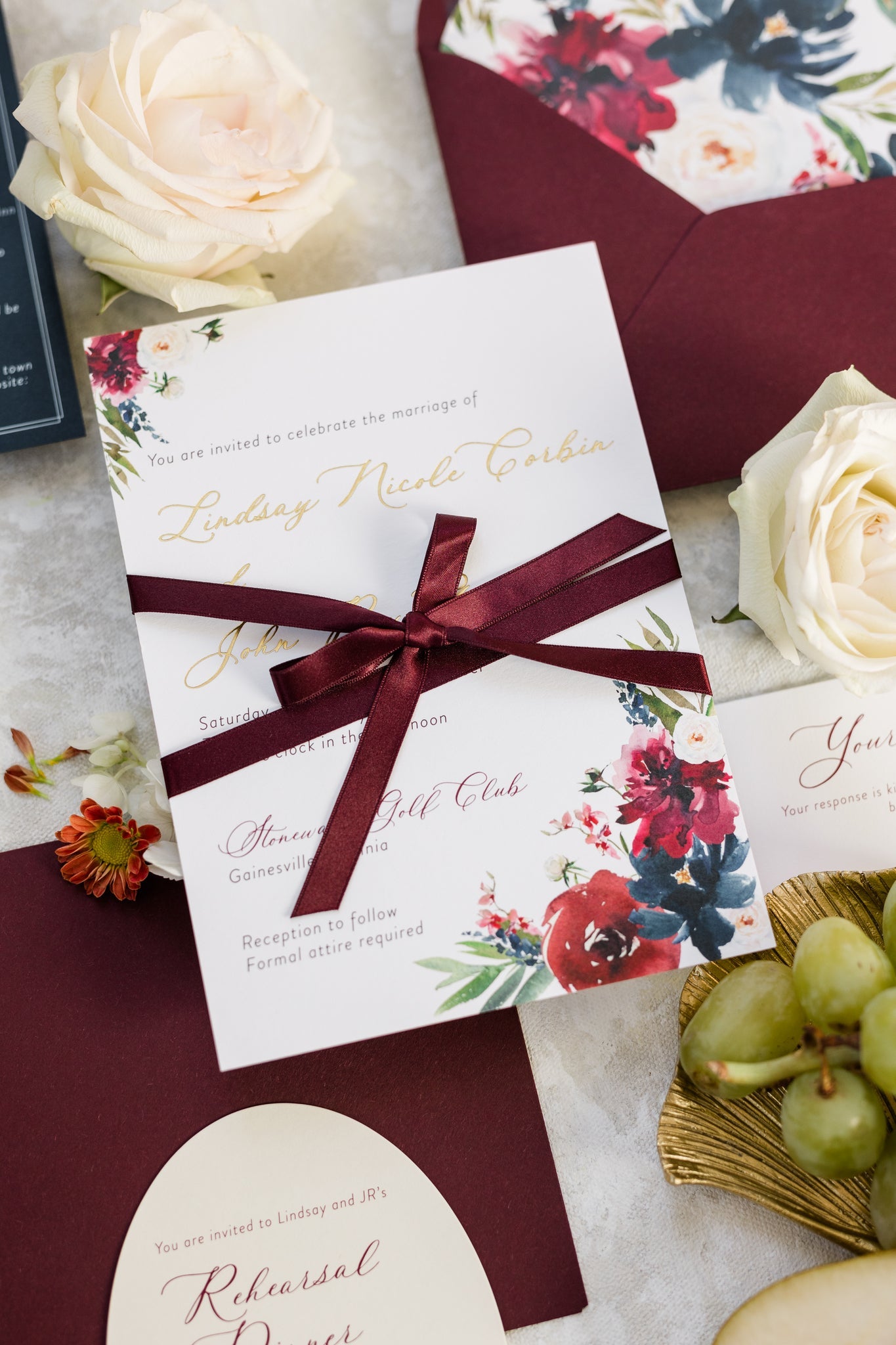 Wedding invitation with a deep red bow tied around it. The couple's name is printed in gold foil.