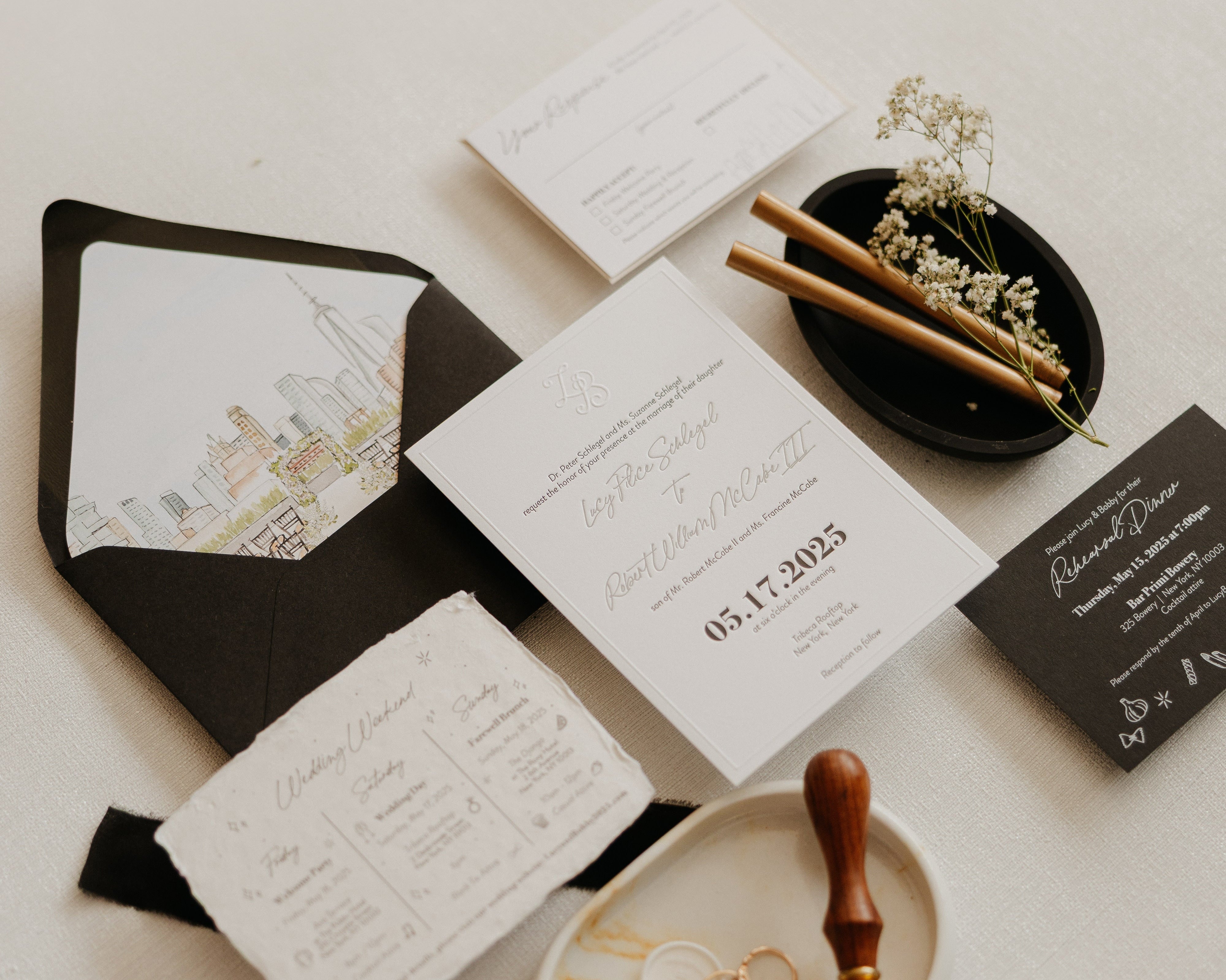 A flat lay of a black and white invitation suite.  The black envelope has a watercolor illustration of the New York City skyline on the inside flap.
