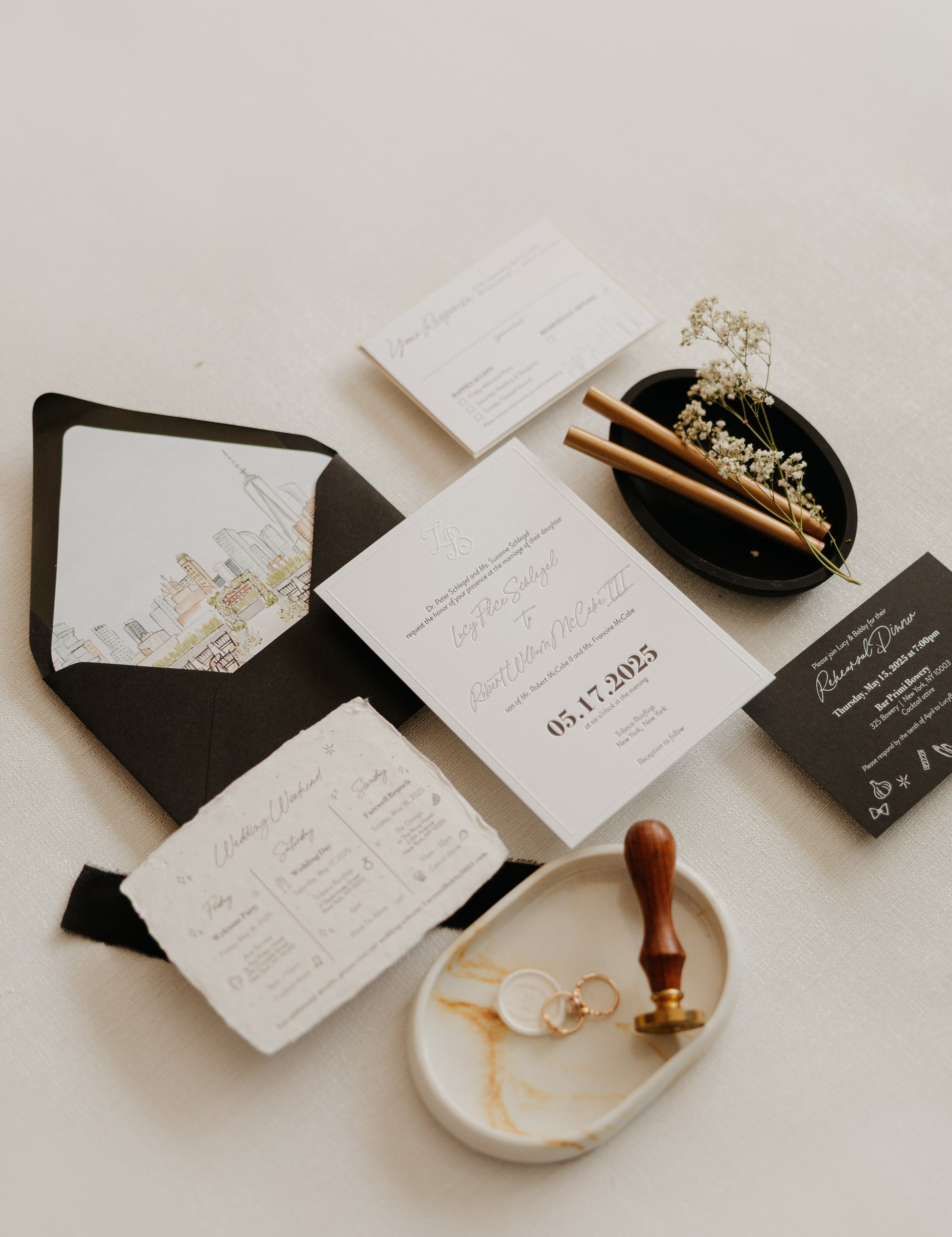 A flat lay of a black and white invitation suite.  The black envelope has a watercolor illustration of the New York City skyline on the inside flap.