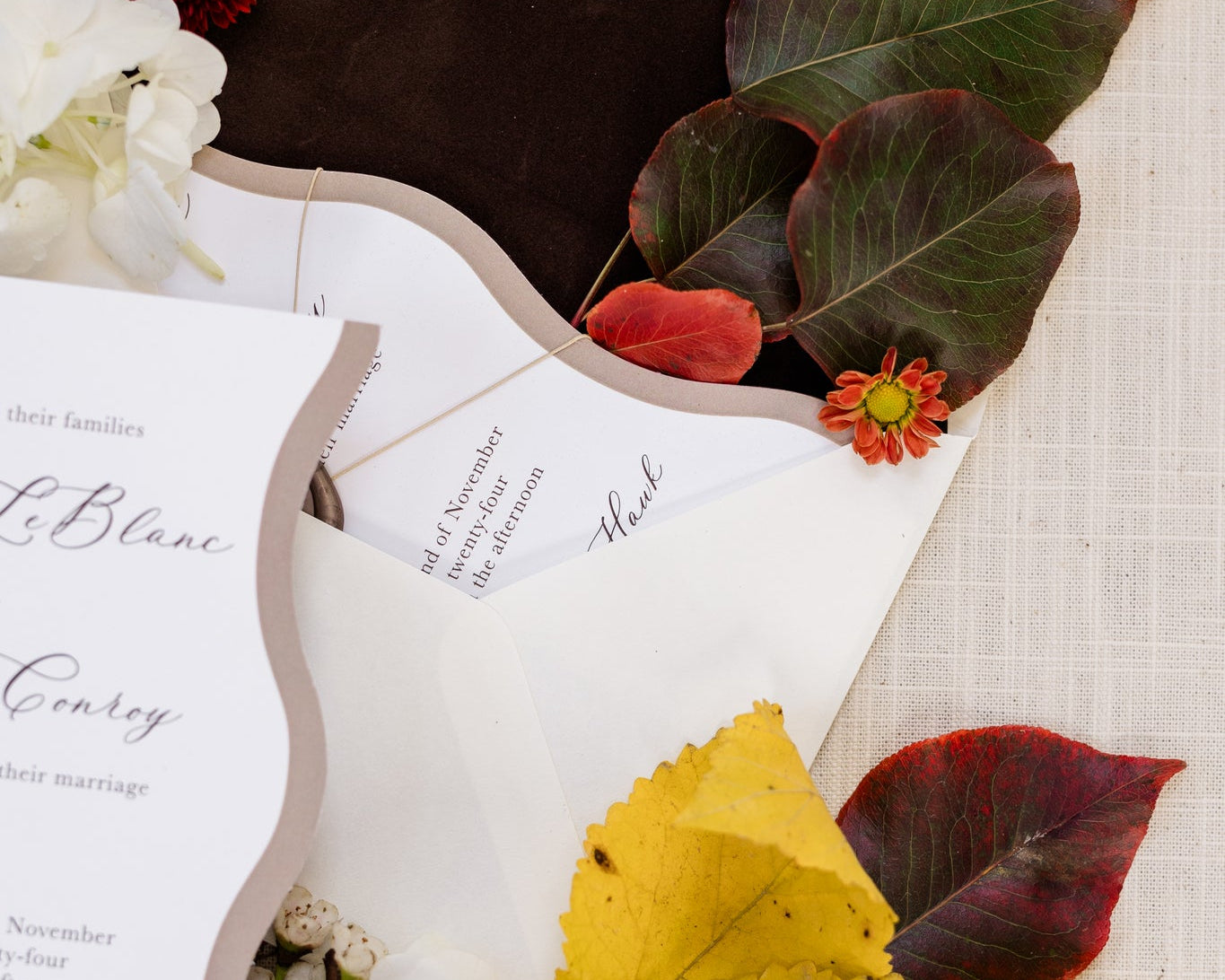 A close up of a dark brown velvet envelope liner.  Colorful leaves with deep greens and reds have been placed inside the envelope..