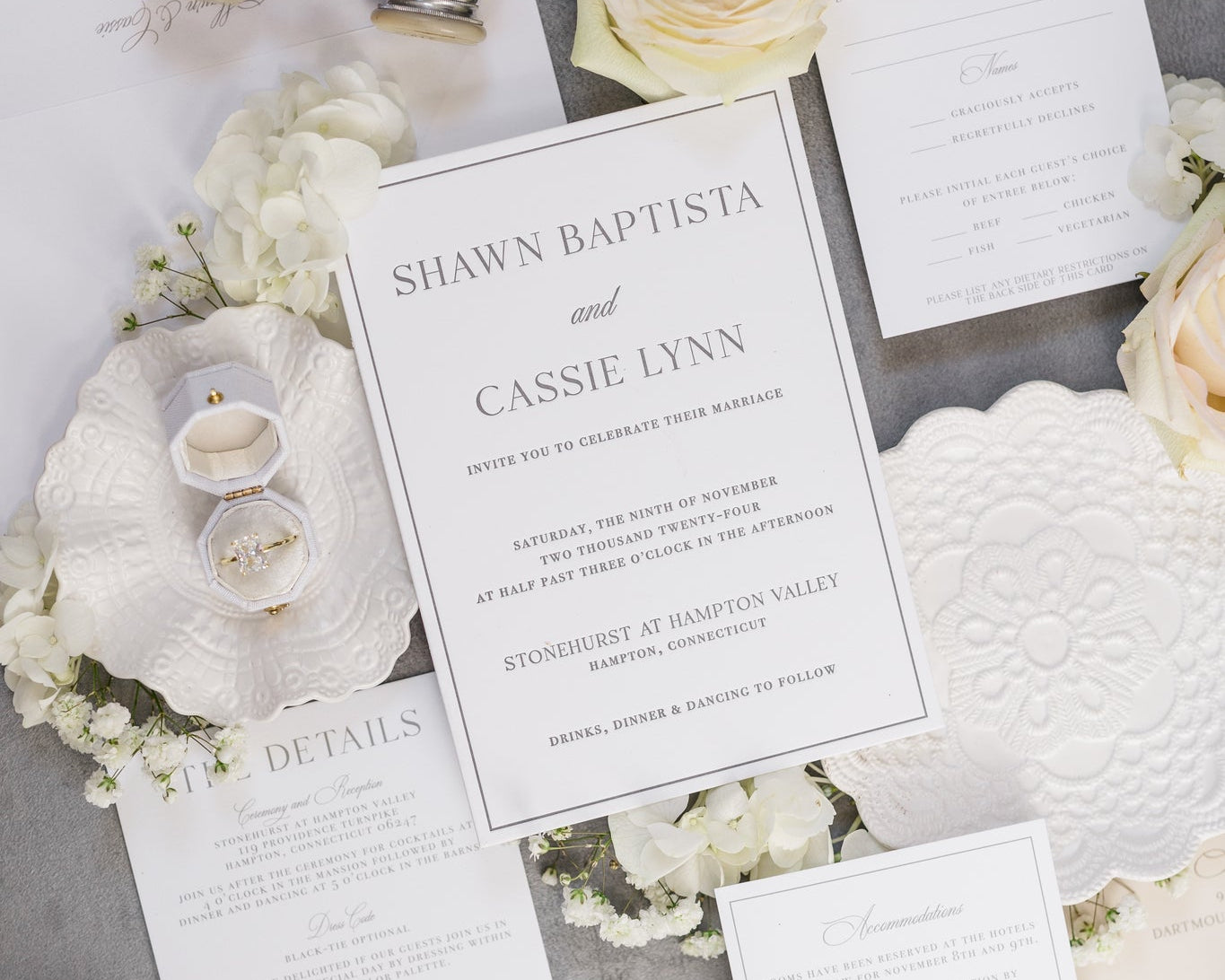 A flat lay of a wedding suite.  The invites are printed on white card stock with simple gray text print.