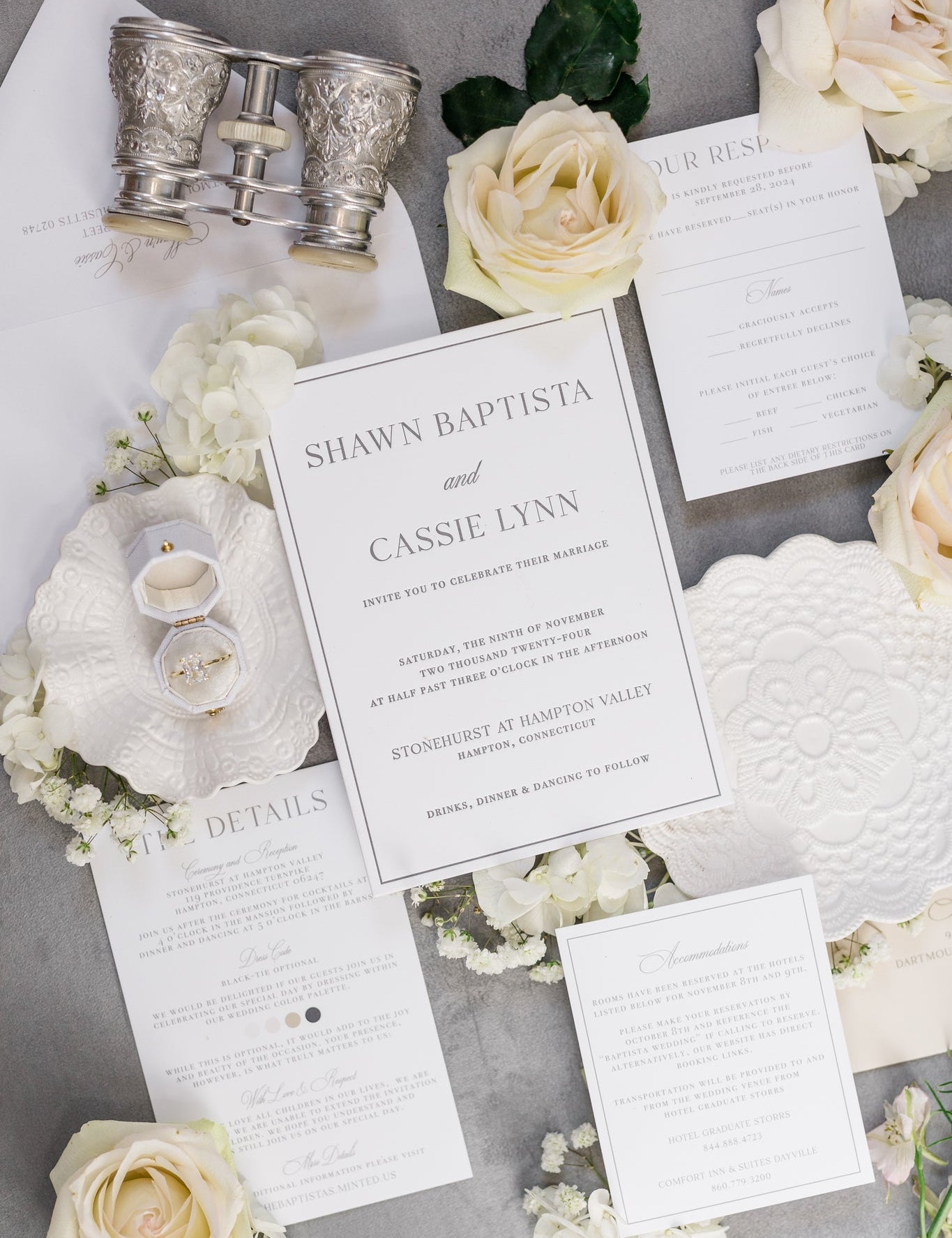 A flat lay of a wedding suite.  The invites are printed on white card stock with simple gray text print.