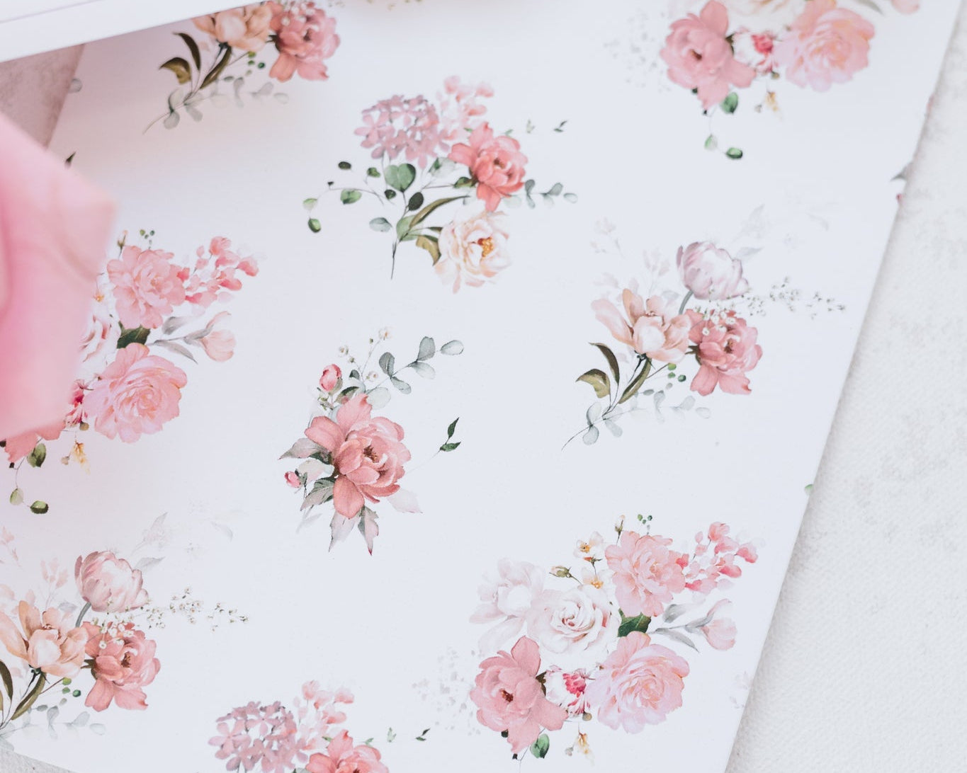 A close up of pink roses and carnations with dainty greenery that is printed on the back of a invitation. 