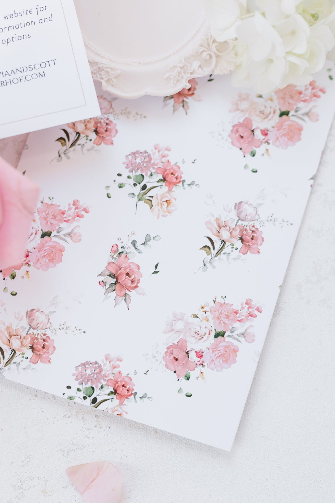 A close up of pink roses and carnations with dainty greenery that is printed on the back of a invitation. 