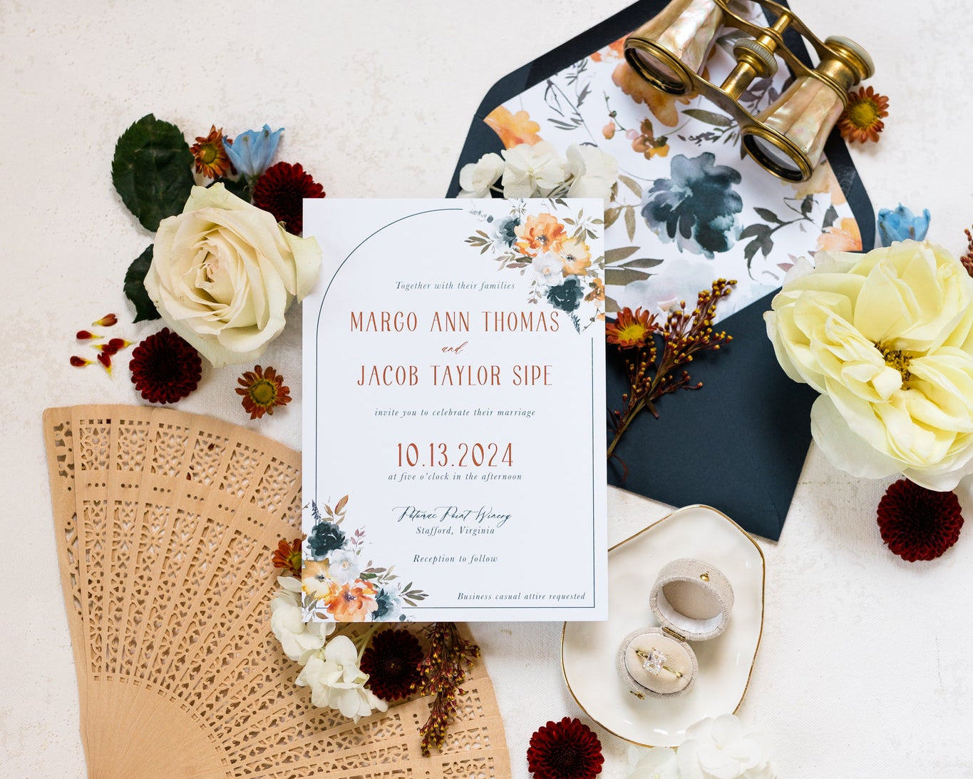 A flat lay of an invitation suite.  The cards features a dark navy envelope with a floral liner and bold orange text on the main invite.