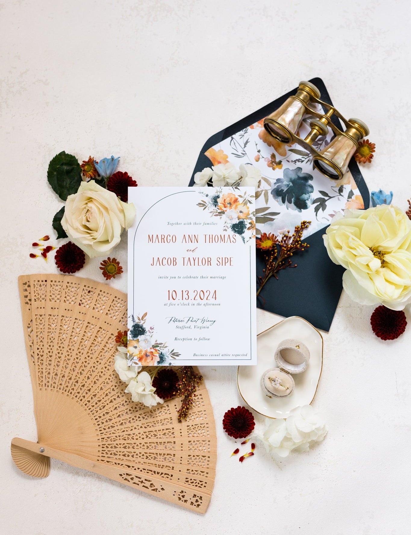 A flat lay of an invitation suite.  The cards features a dark navy envelope with a floral liner and bold orange text on the main invite.