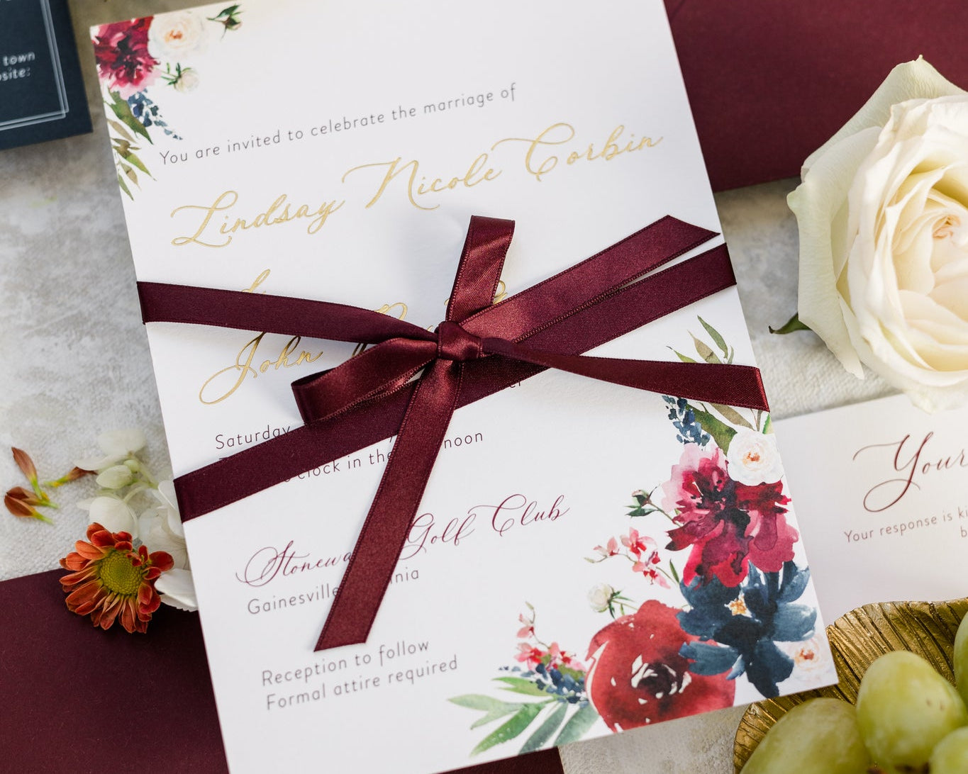 Wedding invitation with a deep red bow tied around it.  The couple's name is printed in gold foil.