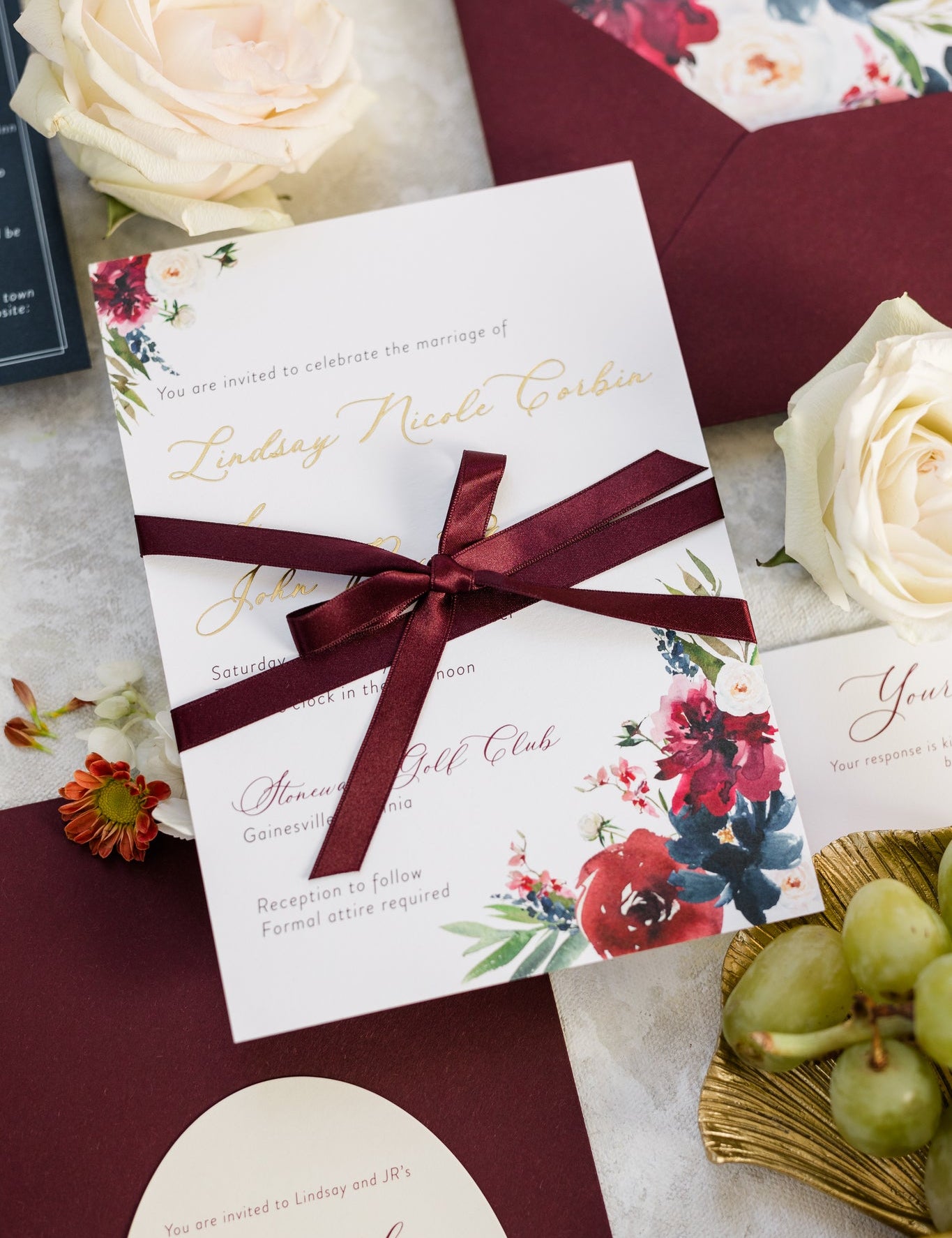 Wedding invitation with a deep red bow tied around it.  The couple's name is printed in gold foil.