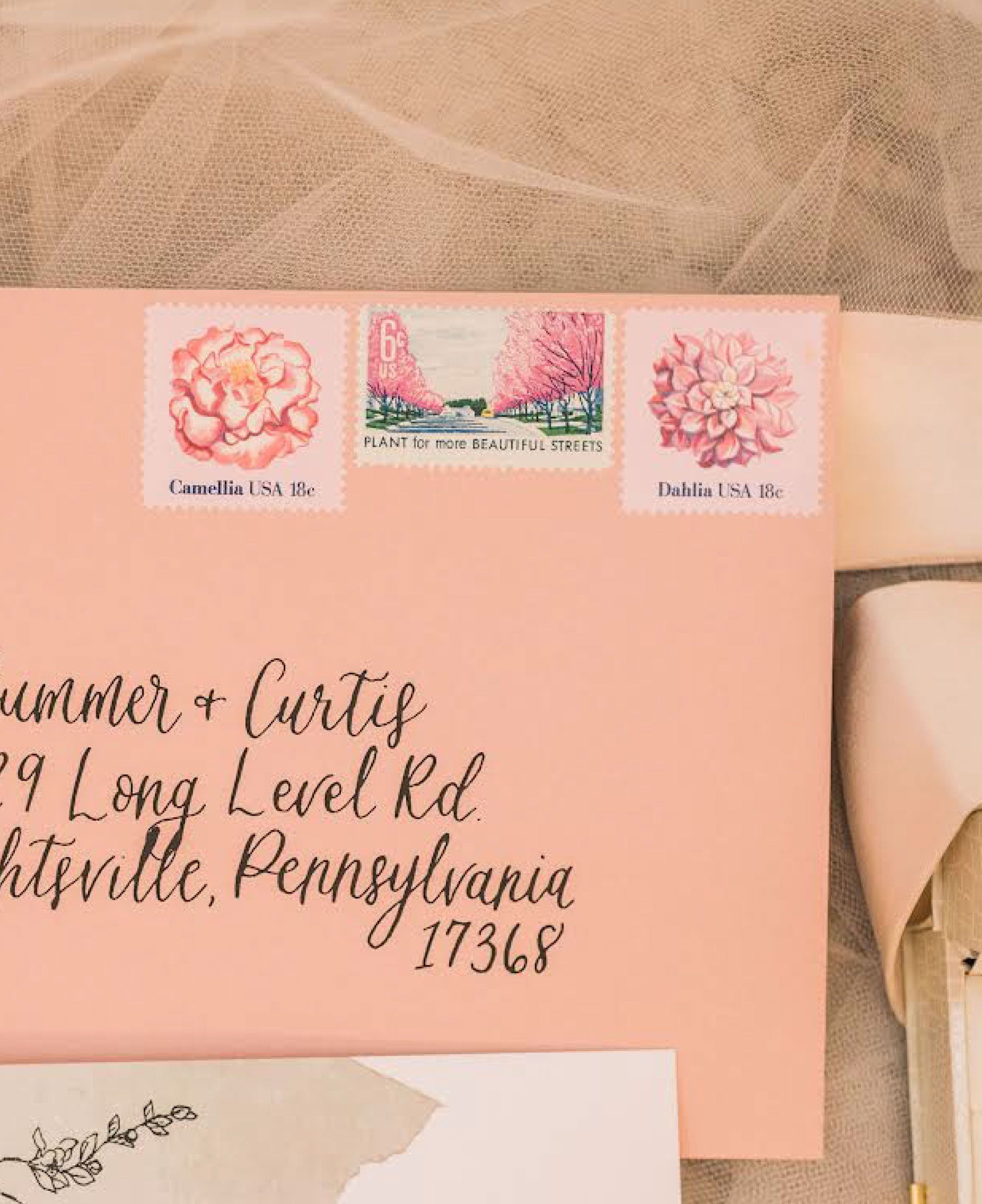 A light pink envelope with three vintage stamps on the top left.  The stamps have illustrations of pink flowers and cherry blossoms.