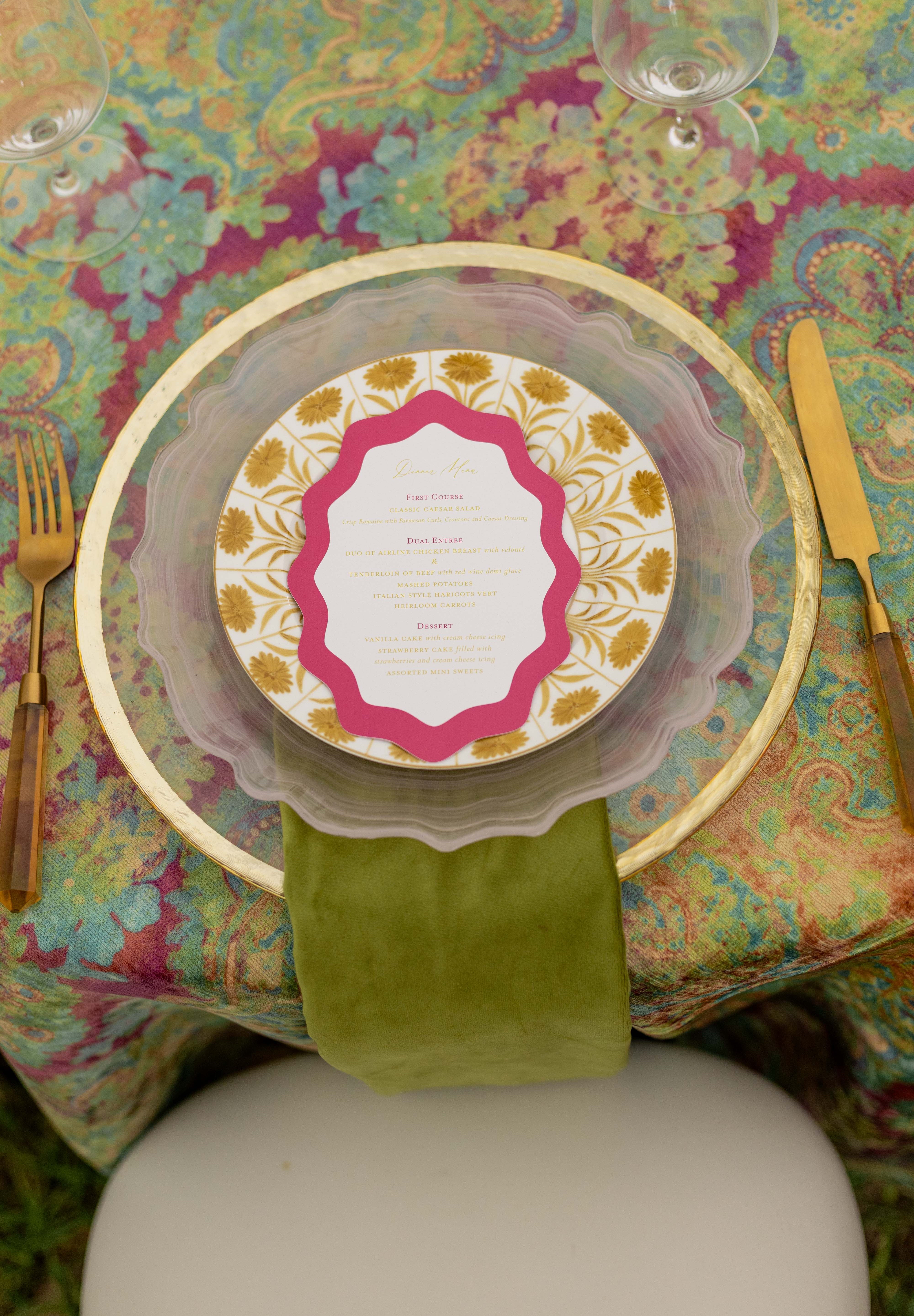 Decorative table setting with a colorful tablecloth, gold cutlery, and a place card.