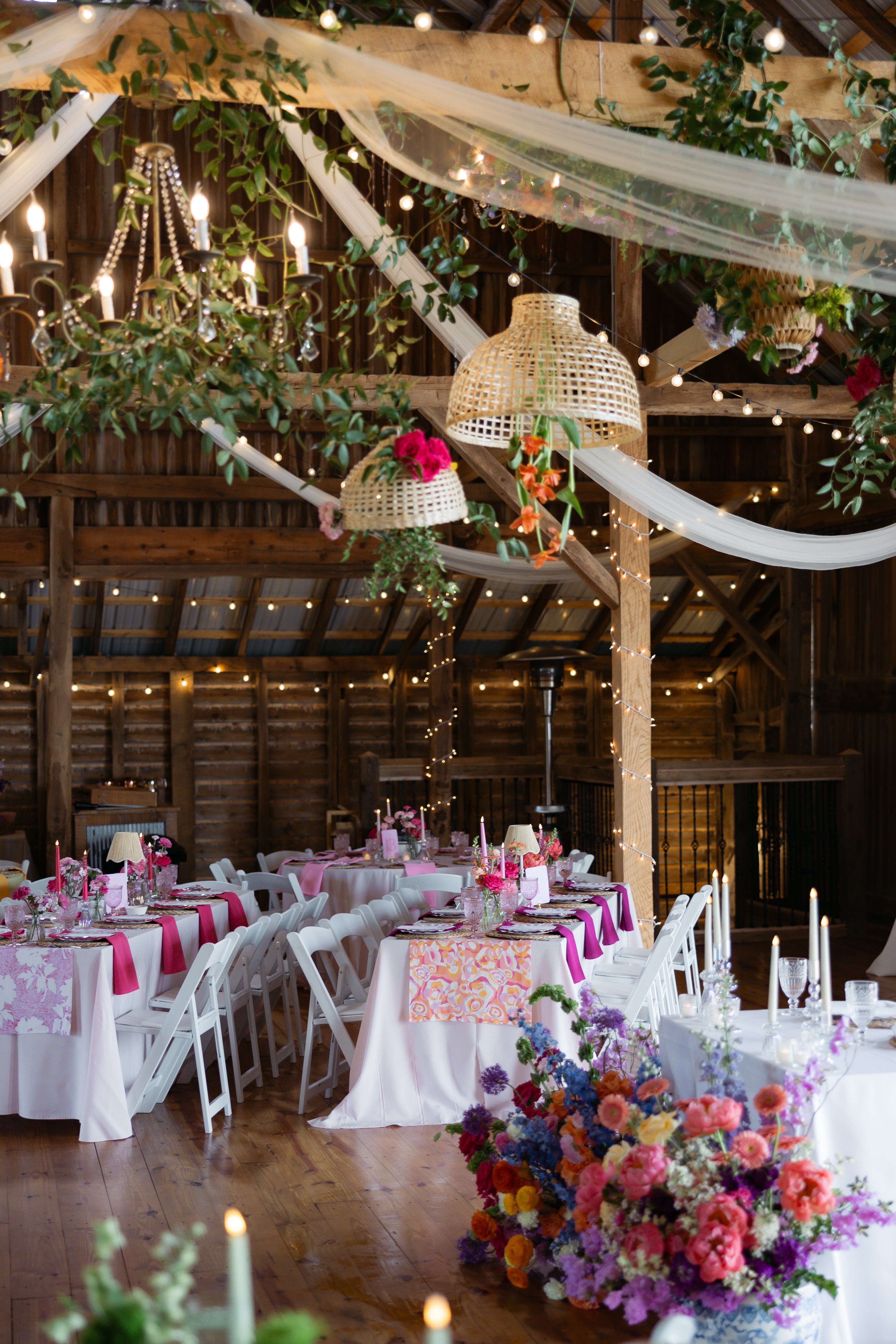 Decorated indoor wedding reception with tables, floral arrangements, and string lights.