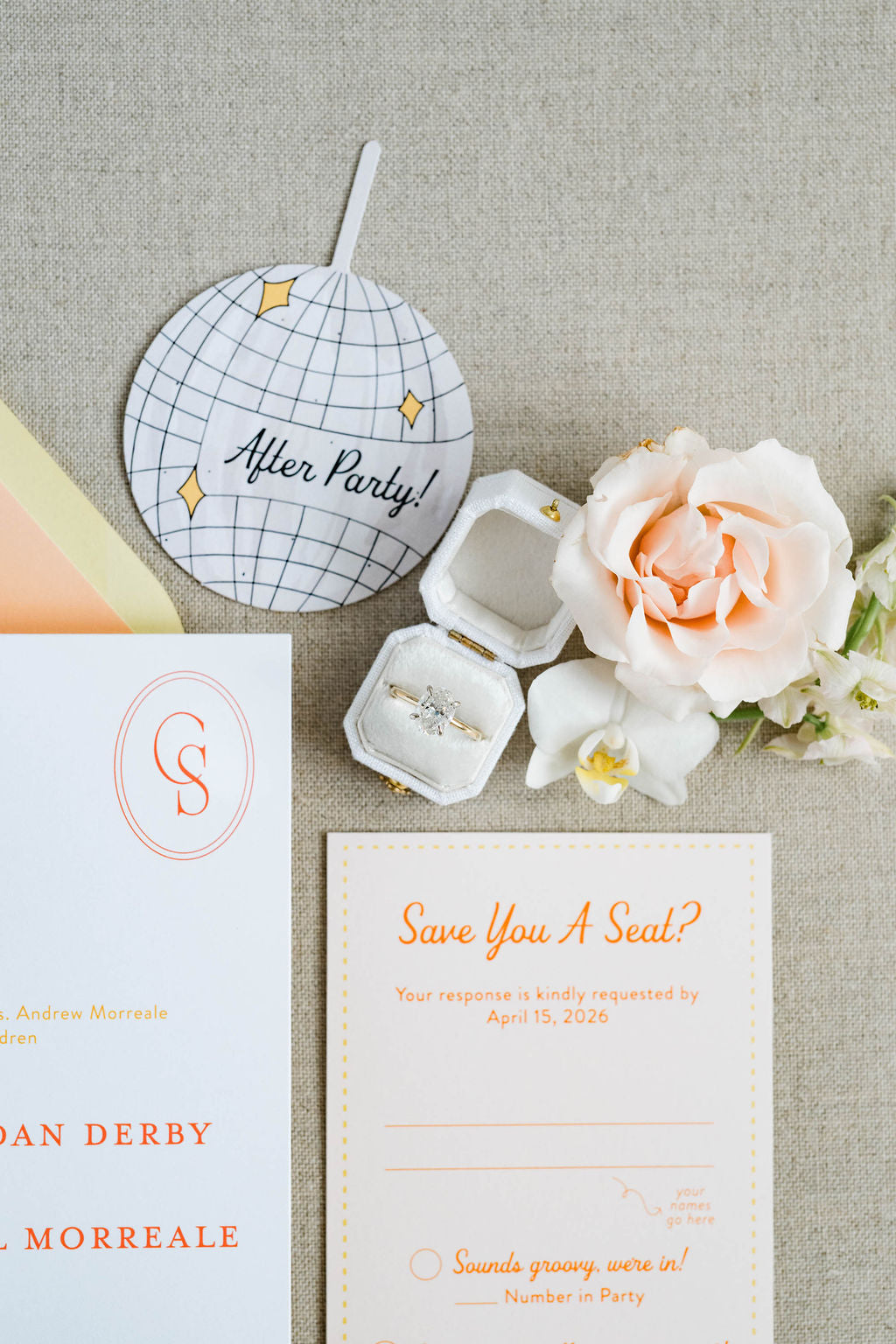 Wedding invitation set with 'After Party!' sign, ring box, and flowers on a textured surface.