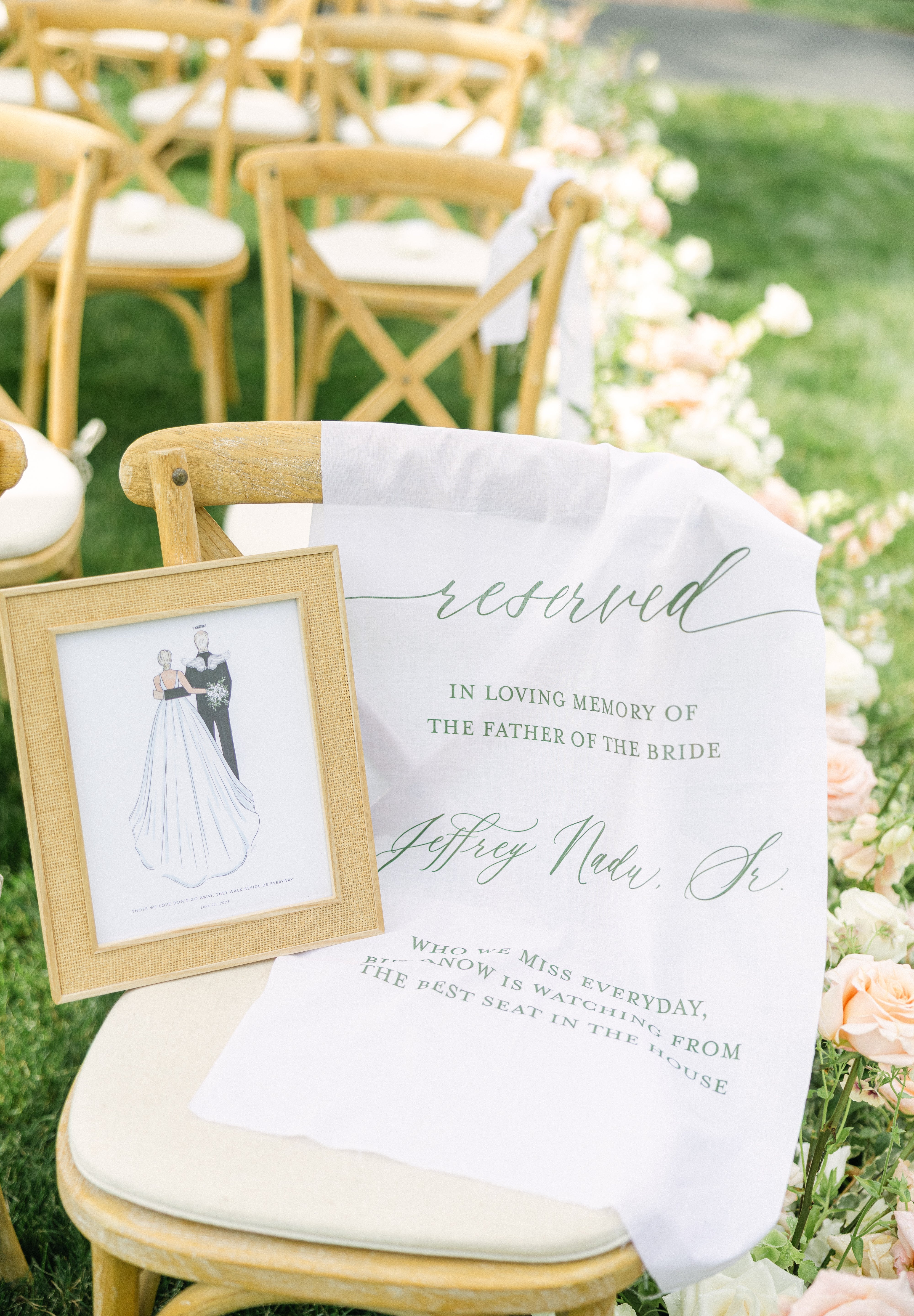 Reserved sign on a chair at an outdoor wedding ceremony with a framed illustration of a couple.