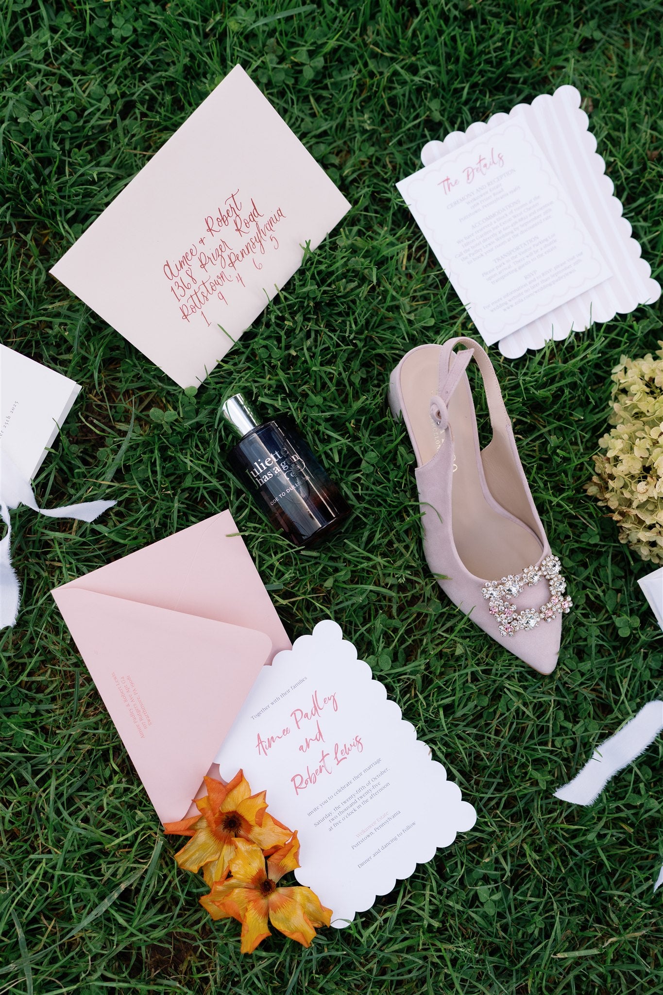 Pink high-heeled shoes, invitation cards, and a bottle on grass