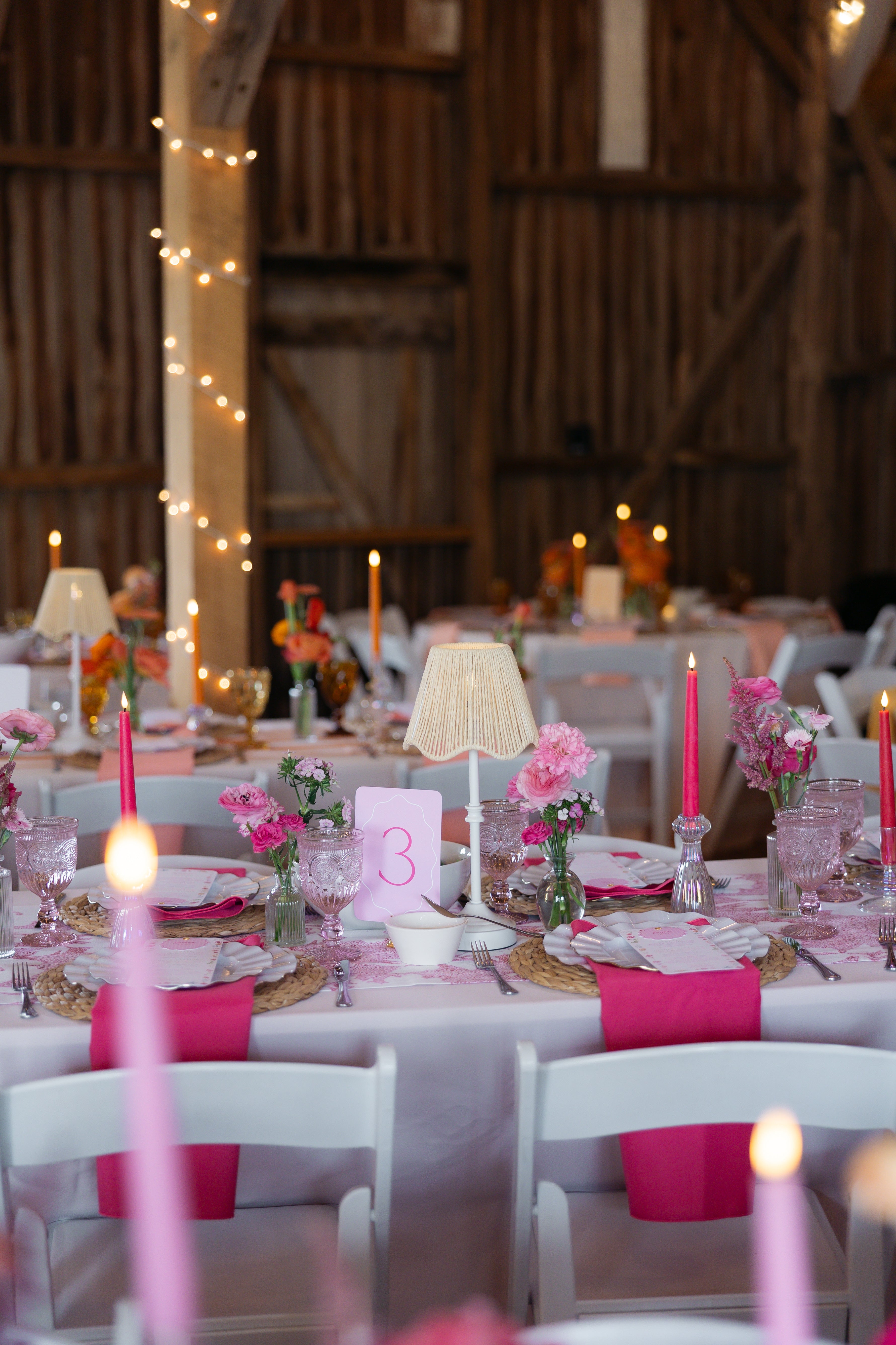 Decorated tables with pink candles and floral arrangements in a rustic barn setting.