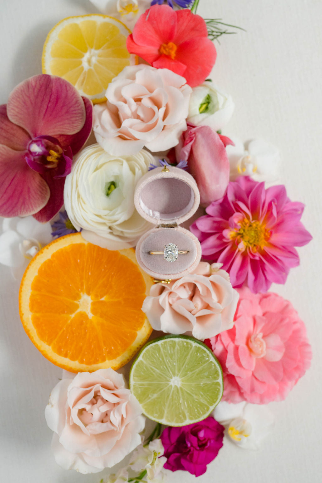 wedding ring box surrounded by colorful flowers and citrus fruits on a white background