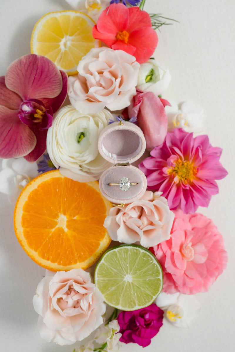 wedding ring box surrounded by colorful flowers and citrus fruits on a white background