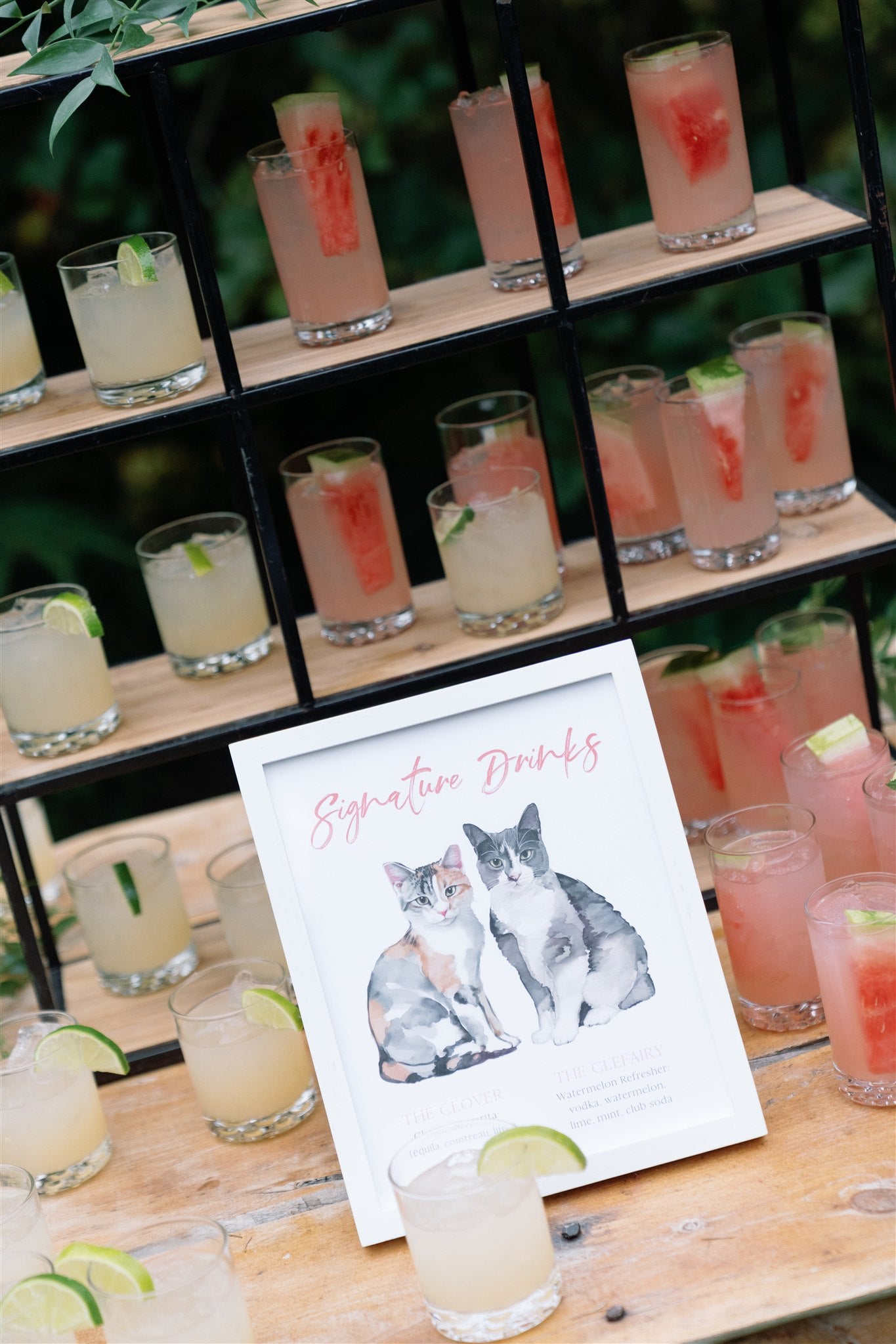 Shelves with glasses of pink drinks and a sign featuring cat illustrations.
